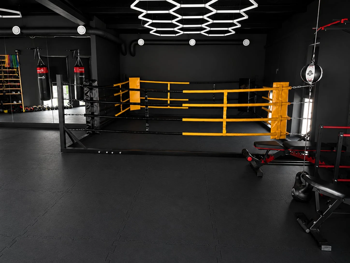 Ring treningowy z żółtymi linami, worki bokserskie i heksagonalne oświetlenie w sali PM Boxing Studio
