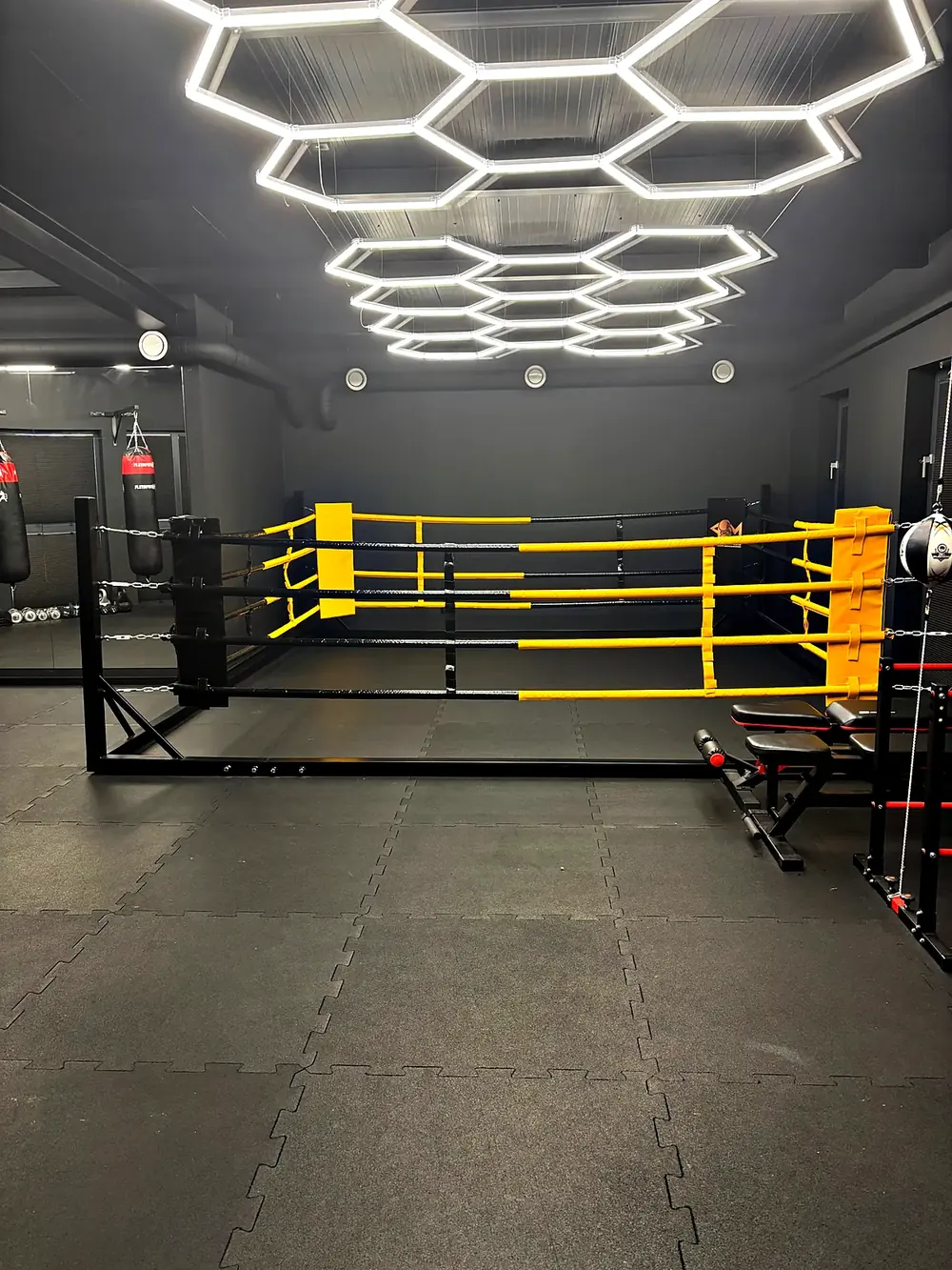 Ring treningowy z żółtymi linami i worki bokserskie w sali PM Boxing Studio
